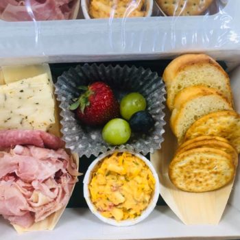A catered box of meats, cheeses, crackers, and fruit.