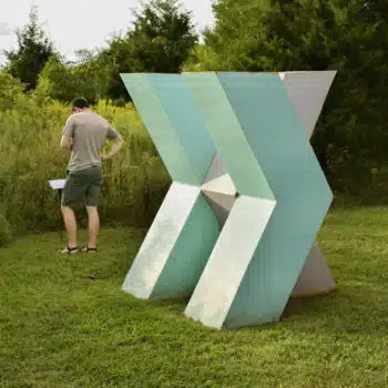 Person reading about a sculpture. Teh sculpture is a light teal, geometric piece of art.