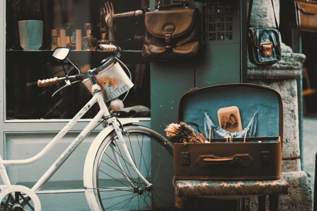 vintage bicycle parked outside storefront, accompanied by an open suitcase holding antique items
