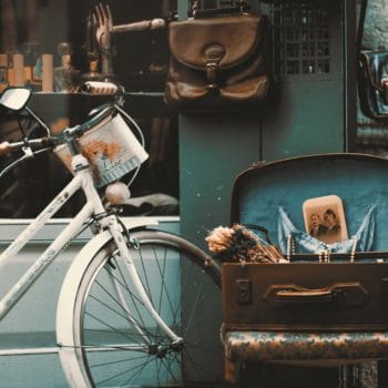vintage bicycle parked outside storefront, accompanied by an open suitcase holding antique items