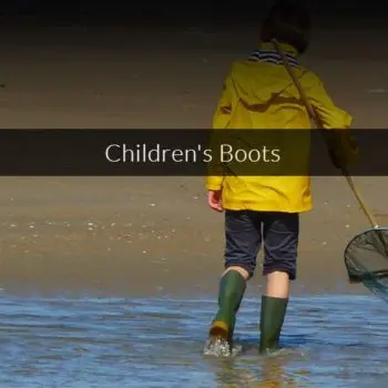 back of kid wearing yellow rain parka and green rain boats holding a fishing net, wading through water