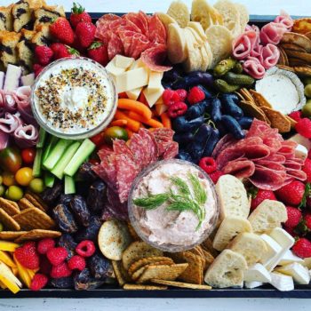 Charcuterie board. Includes strawberries, raspberries, hummus, breads, crackers, salami, carrots, olives, other cheeses and meats.
