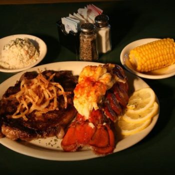 image of plate with steak and lobster tail, dish of corn cob and mashed potatoes, salt and pepper shakers