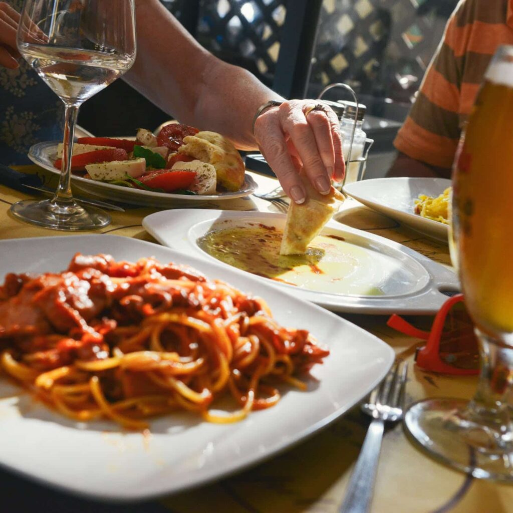 Spaghetti in foreground, plates of bread dipping in oil, vegetables in background