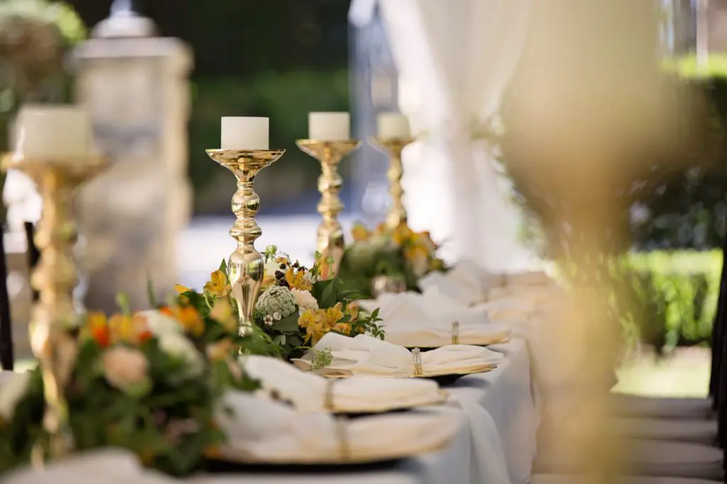 banquet table with gold candle holders, white pillar candles , china, floral arrangements and blurred out background
