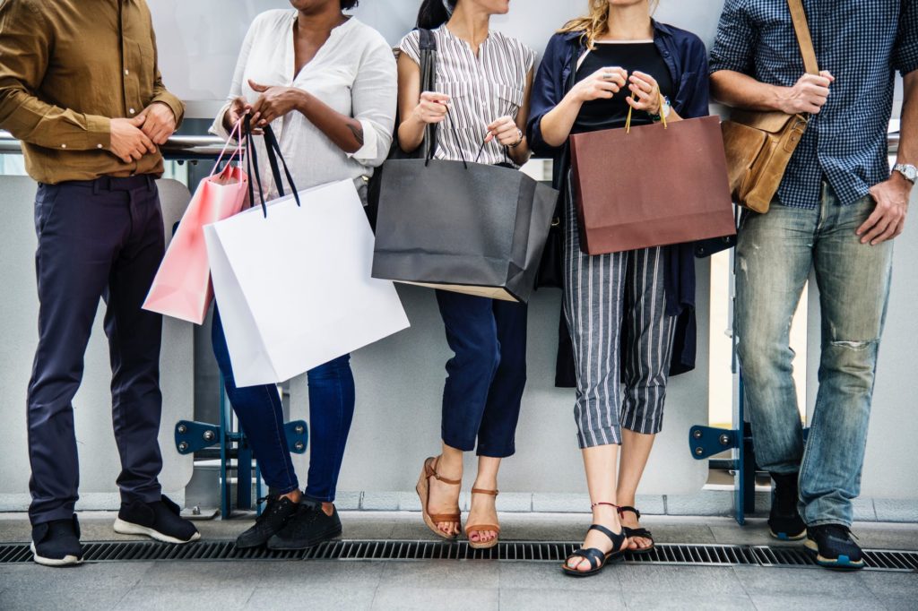 shopping bags of different shapes, colors and sizes held by people of different genders and ethnicity
